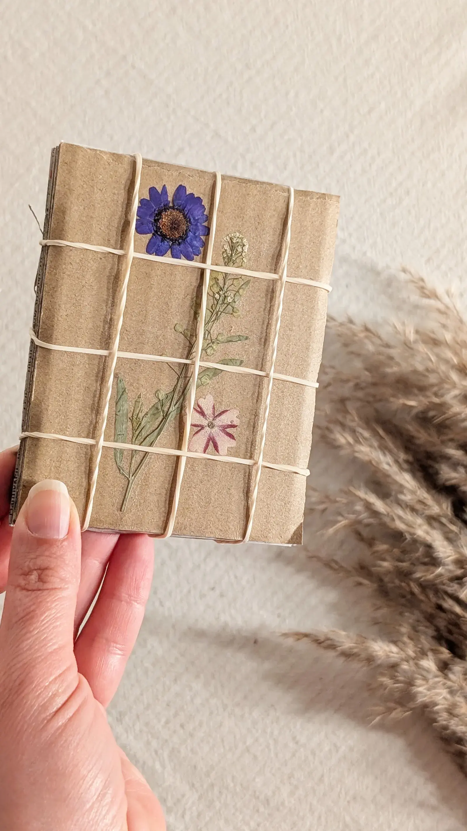 Small handmade pocket flower press made from cardboard, newspaper, and rubber bands with pressed flowers inside.
