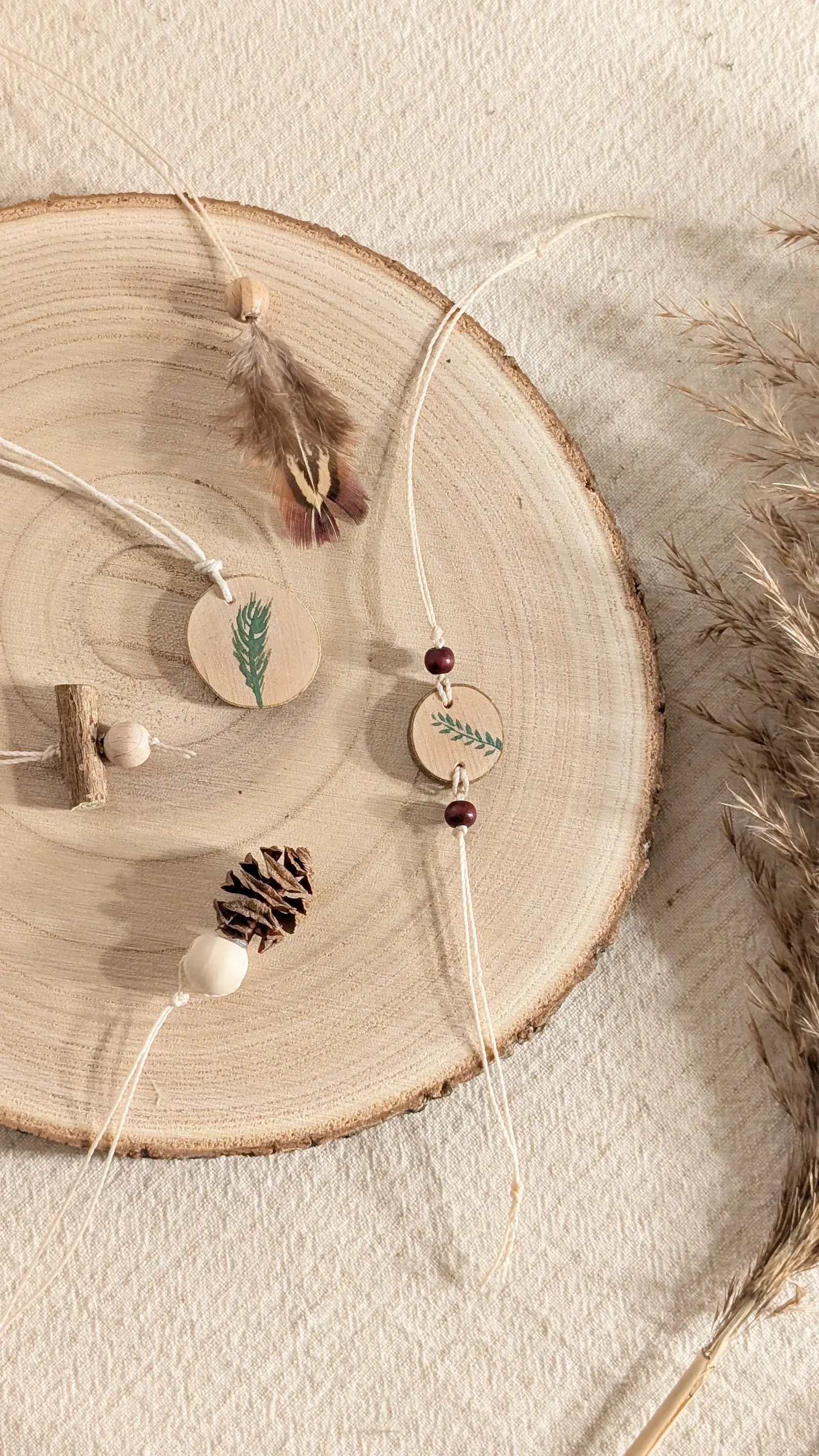 Handmade nature jewelry made from feathers, wood slices, twigs, and natural materials arranged as necklaces and bracelets.