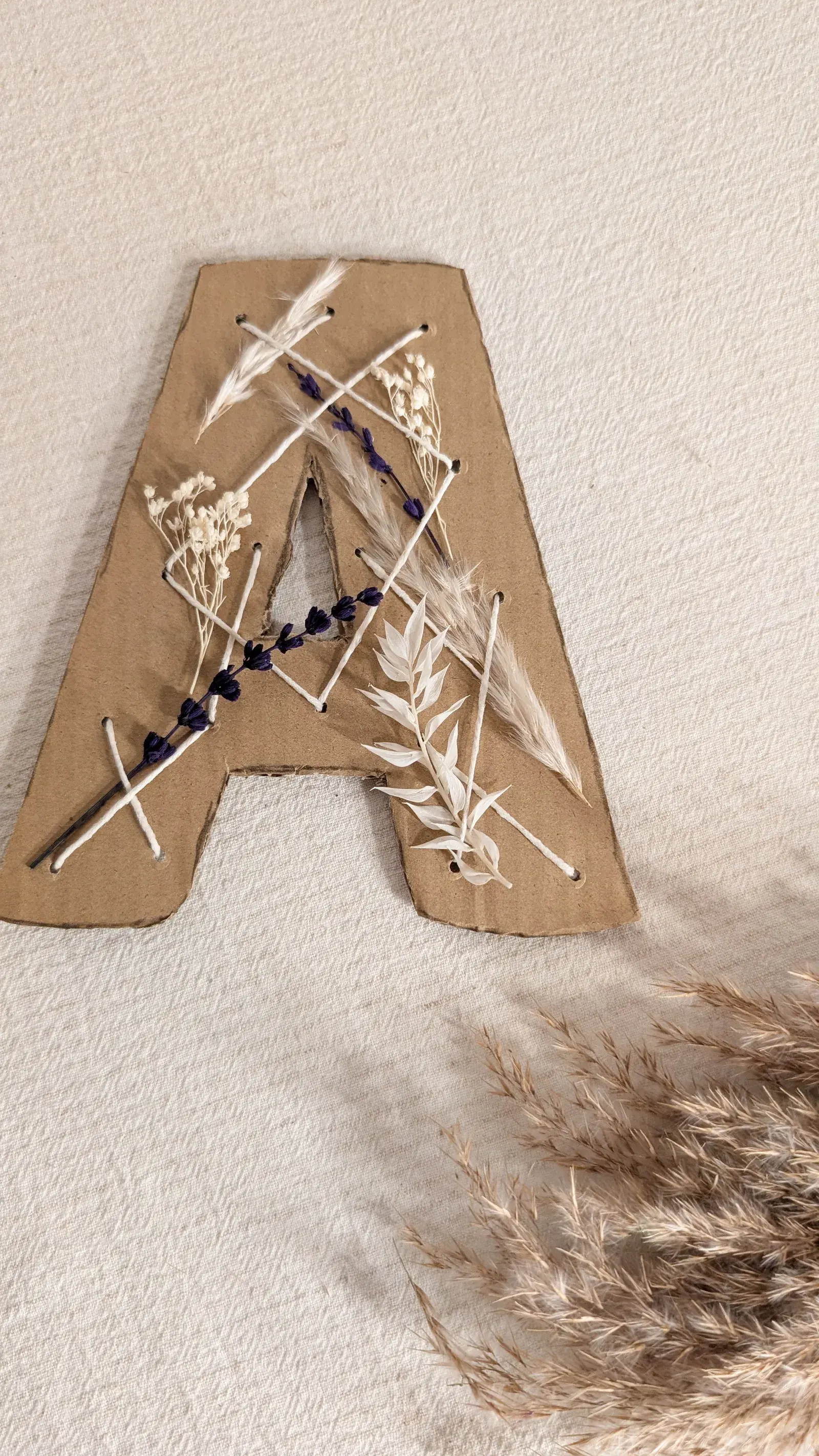 Cardboard initial woven with string and decorated with dried flowers and natural materials.