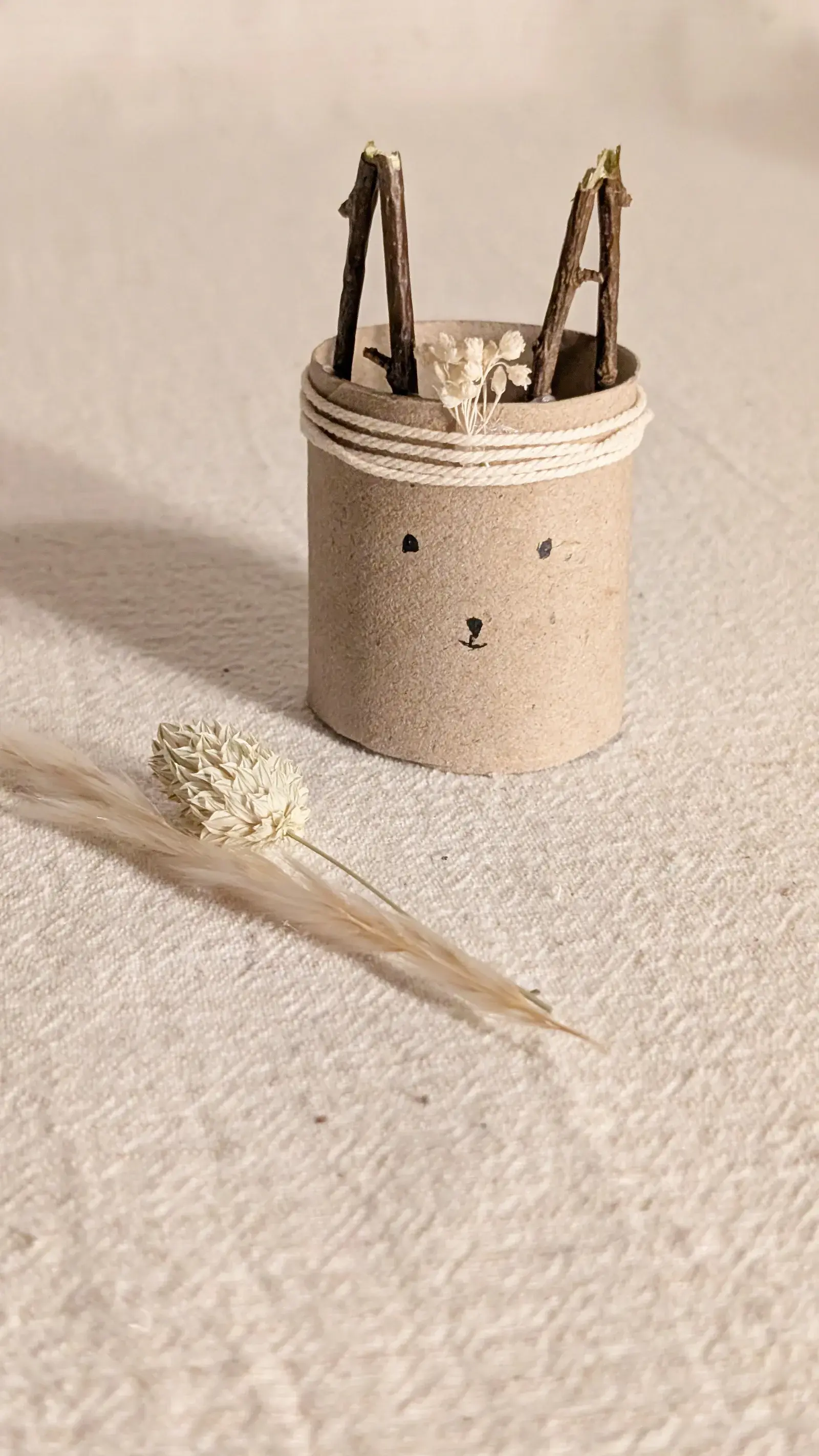Handmade rabbit made from a toilet paper roll with twig ears, dried flowers, and a twine scarf.