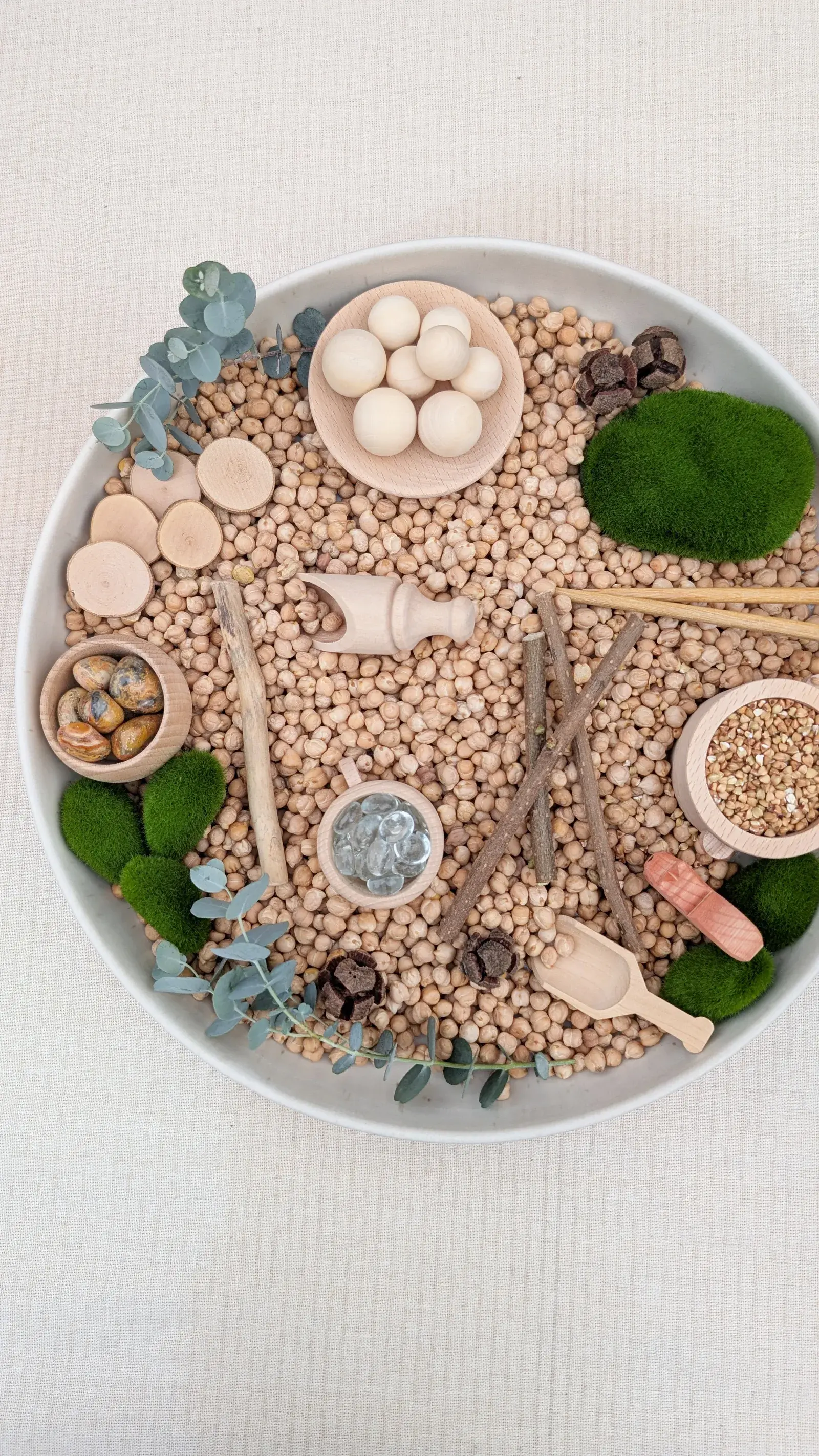 Woodland sensory play tray filled with moss, pinecones, leaves, wooden animals, lentils, and natural materials.